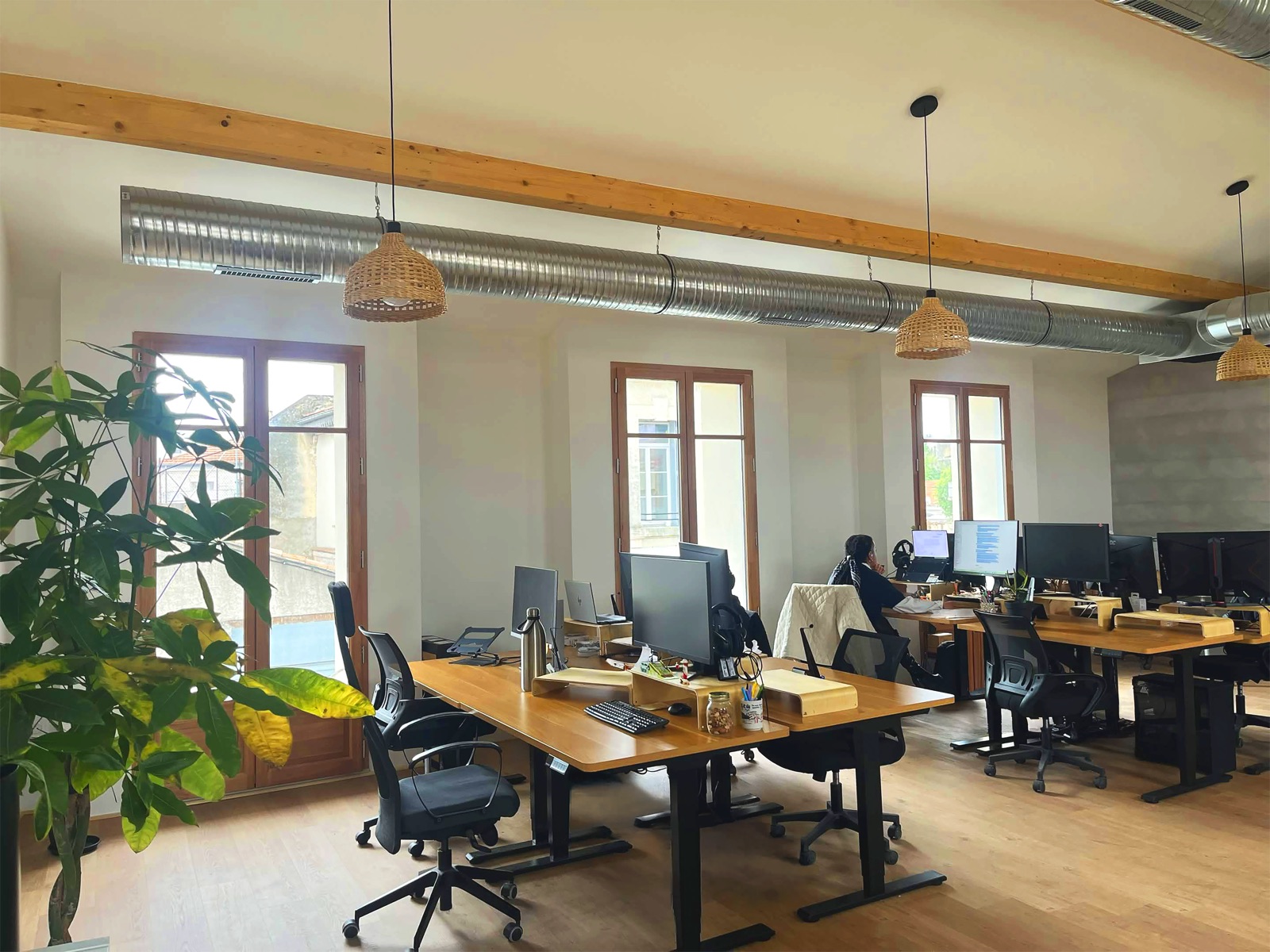 Le plateau du haut des bureaux Multani, poutre apparente, bureaux réglables en bois et grandes fenêtres